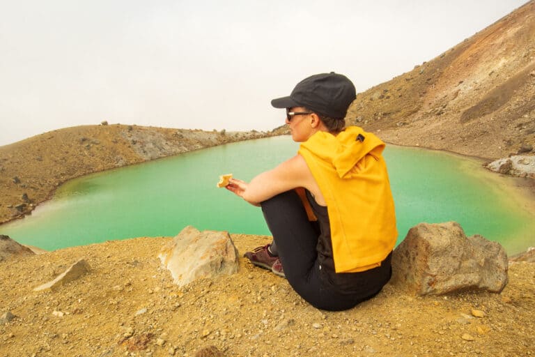 woman sitting in front of green lake eating quiche